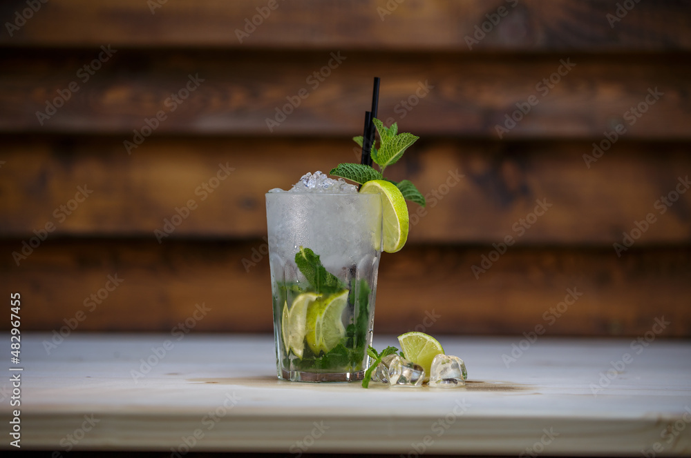 Fresh cold Mojito cocktail with lime and mint and crushed ice on table with wood background