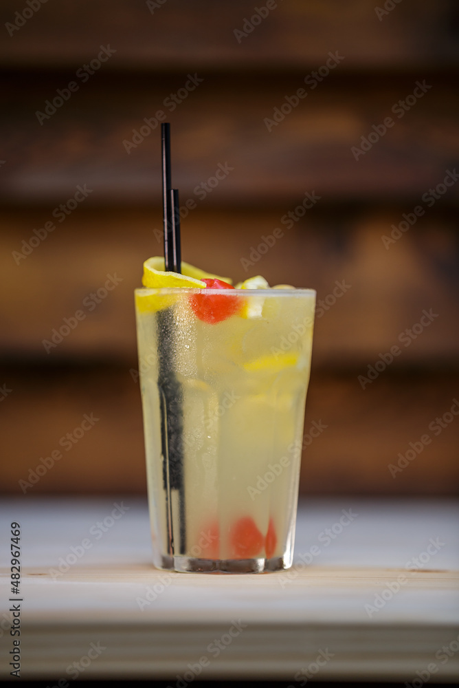 Fresh cold cocktail with lemon and cherry on table with wood background