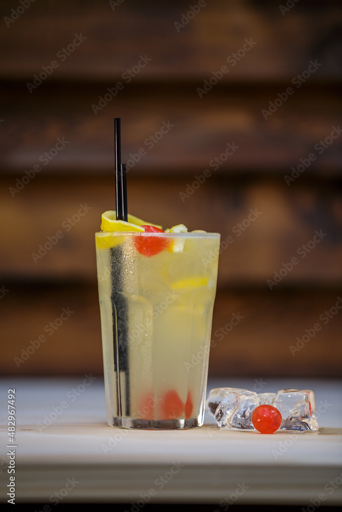 Fresh cold cocktail with lemon and cherry on table with wood background