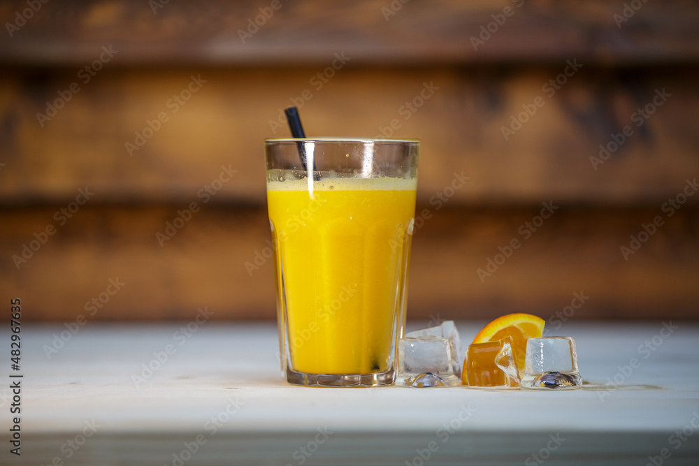 Fresh orange juice with crushed ice and straw on table with wood background