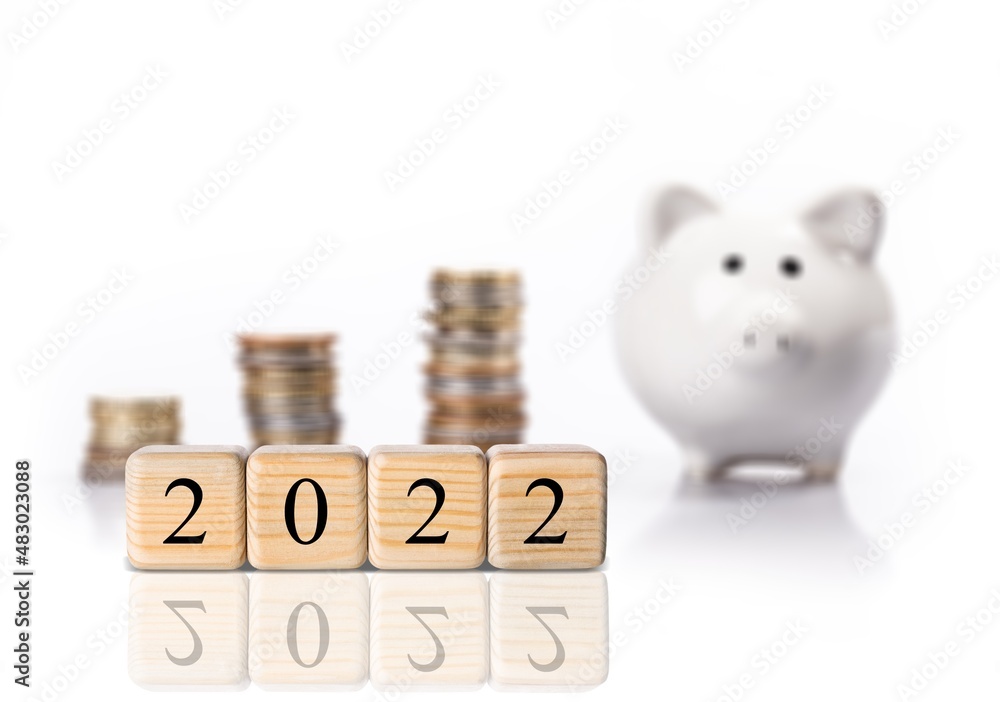 Text of 2022 number written on wooden blocks with blur of coins and piggy bank