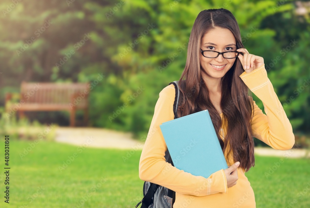 女学生站在户外，手里拿着书。