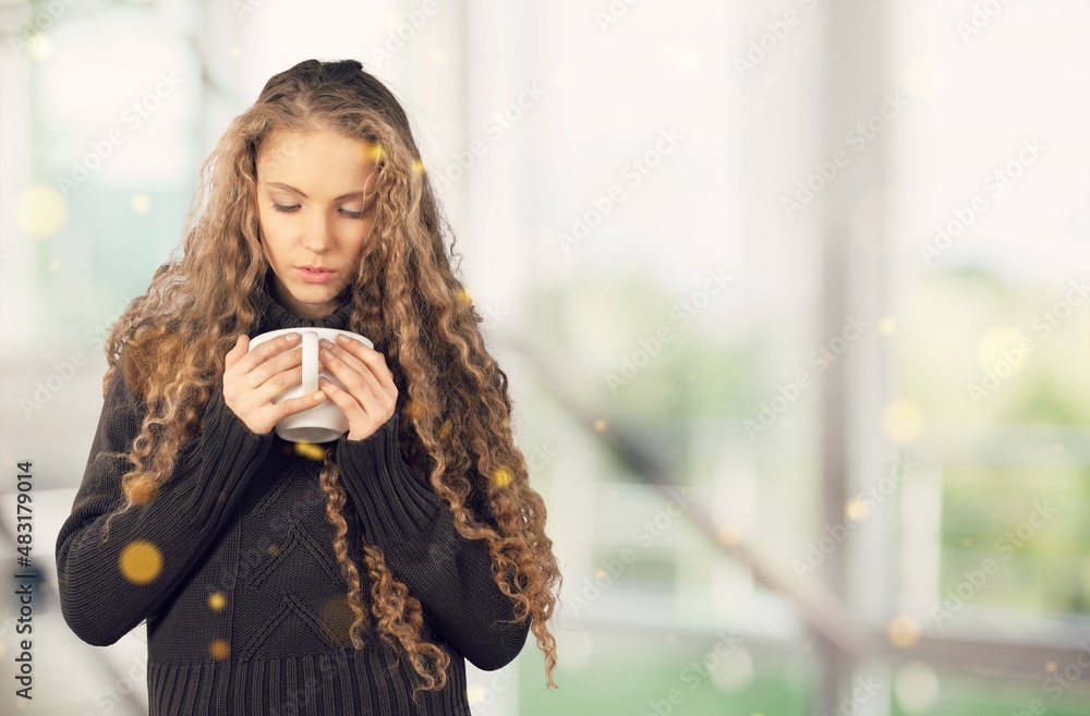 一个美丽的女孩在窗户和灯光的背景下喝茶或喝咖啡。