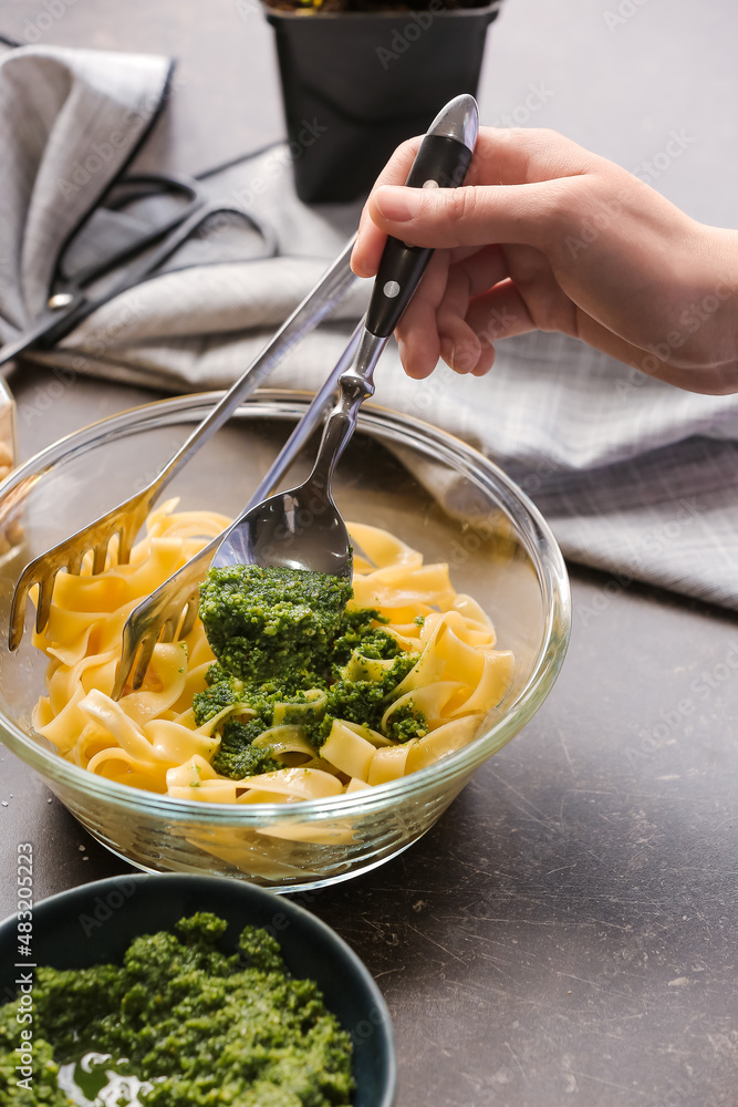 Woman adding pesto sauce in pasta on table in kitchen