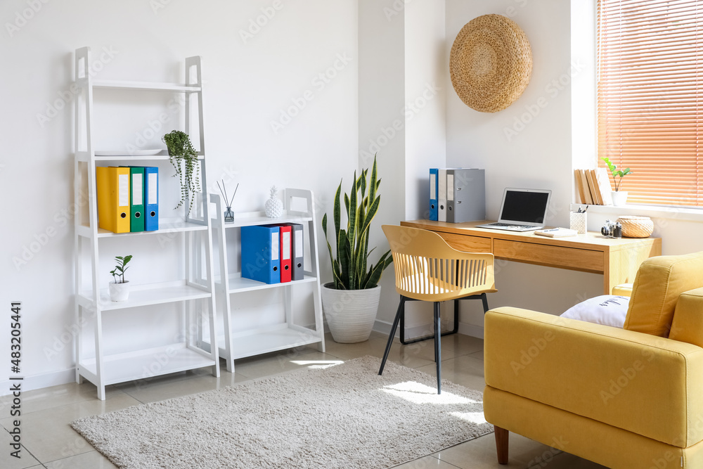 Interior of light office with shelving unit and modern workplace