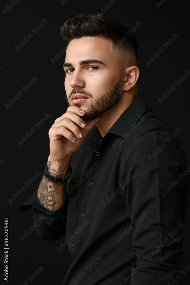 Man with stylish manicure touching his face on black background