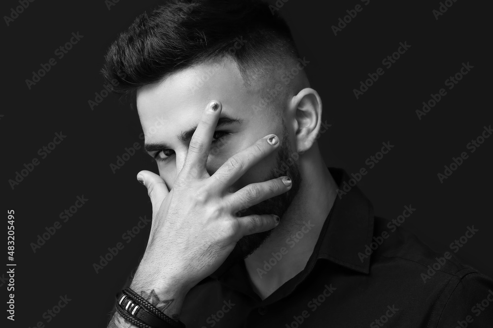 Portrait of man with stylish manicure closing his face with hand on dark background