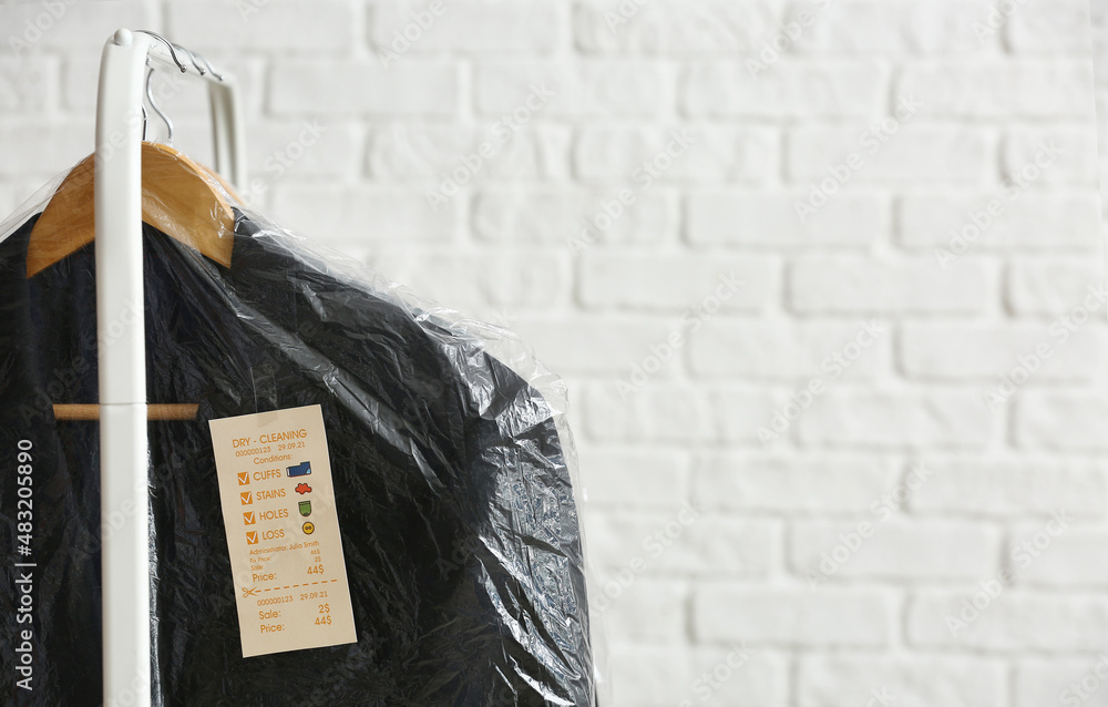 Rack with clean black jackets in plastic bags on white brick background, closeup