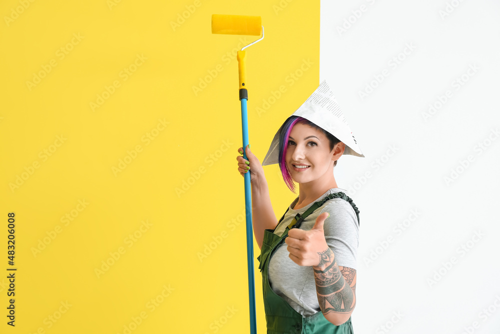 Female painter with paper hat and roller showing thumb-up near color wall