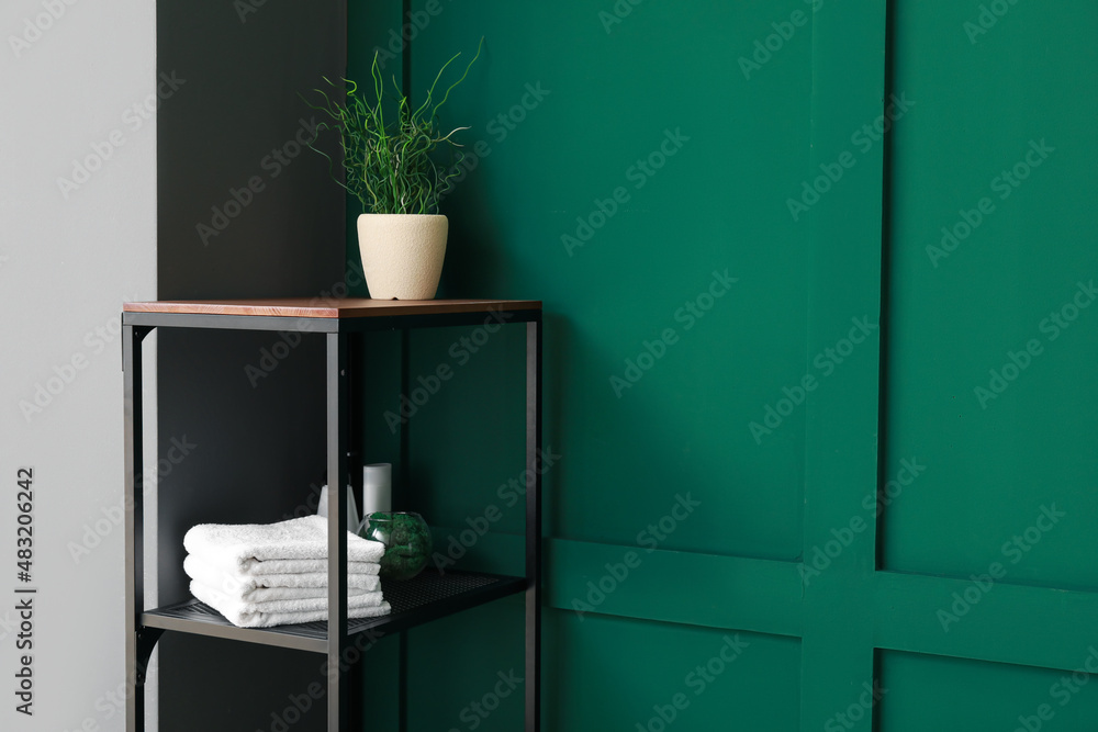 Shelf unit with towels and houseplant near color wall, closeup