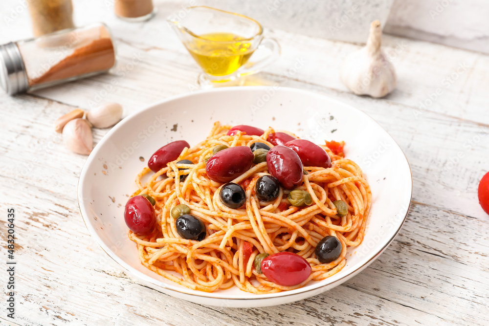 Plate of tasty Pasta Puttanesca on white wooden background