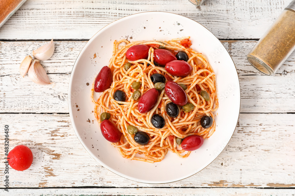 Plate of tasty Pasta Puttanesca on white wooden background