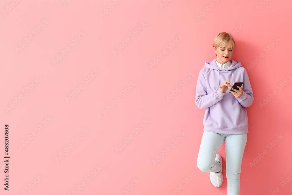 Beautiful young woman in stylish hoodie and with phone on color background