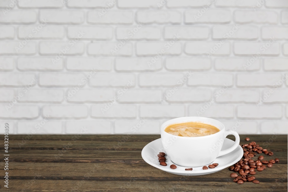 In front of a wall, on a desk, a cup of turkish coffee,  beans.