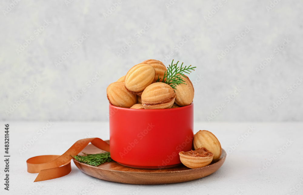 Bowl of tasty walnut shaped cookies with boiled condensed milk on light background