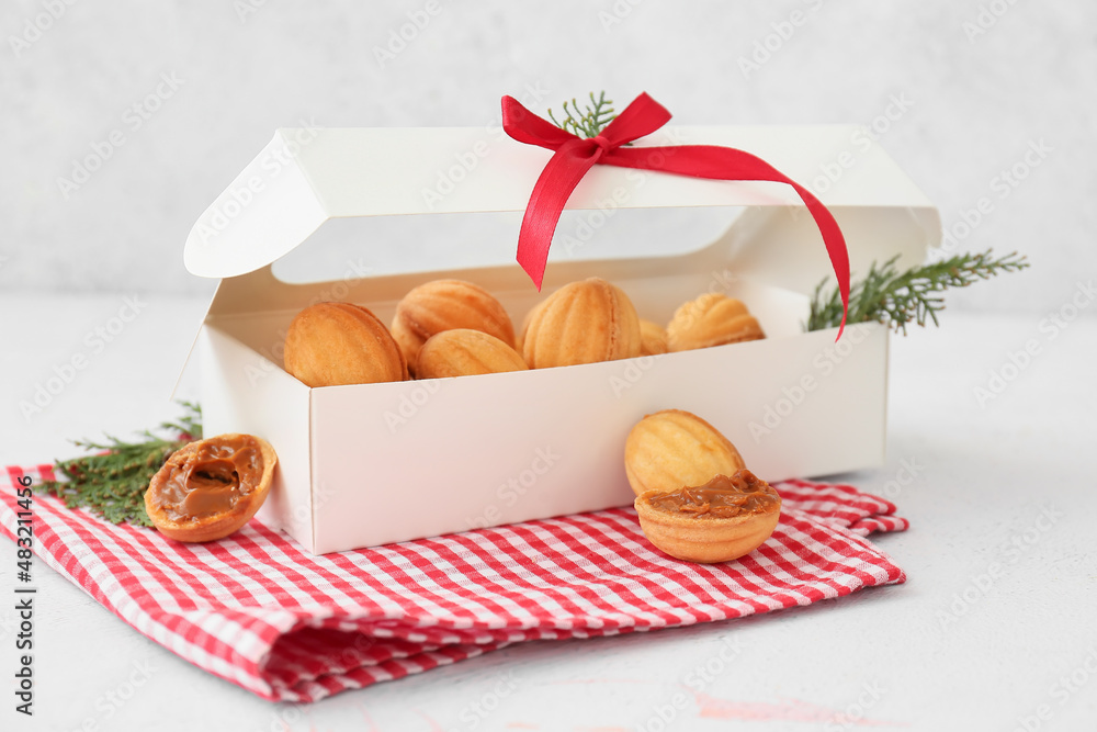 Box with tasty walnut shaped cookies with boiled condensed milk and thuja branches on light backgrou