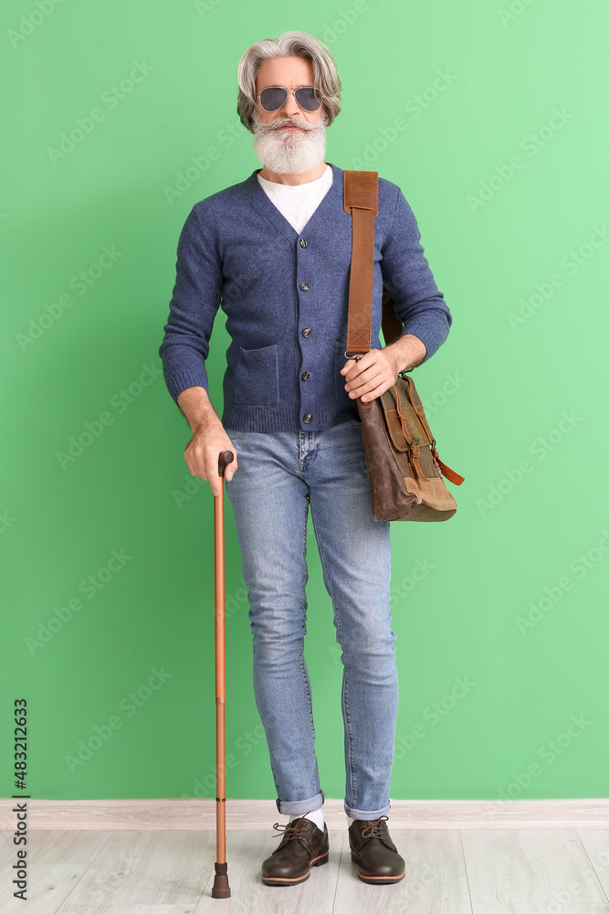 Senior man with walking stick near green wall