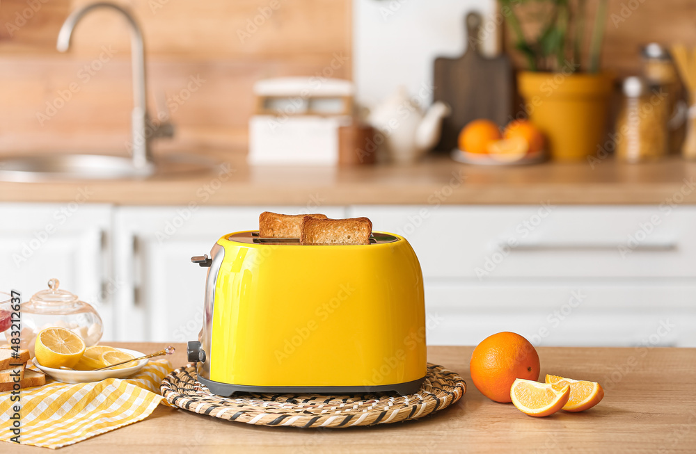 Yellow toaster with bread and orange slices on table in kitchen