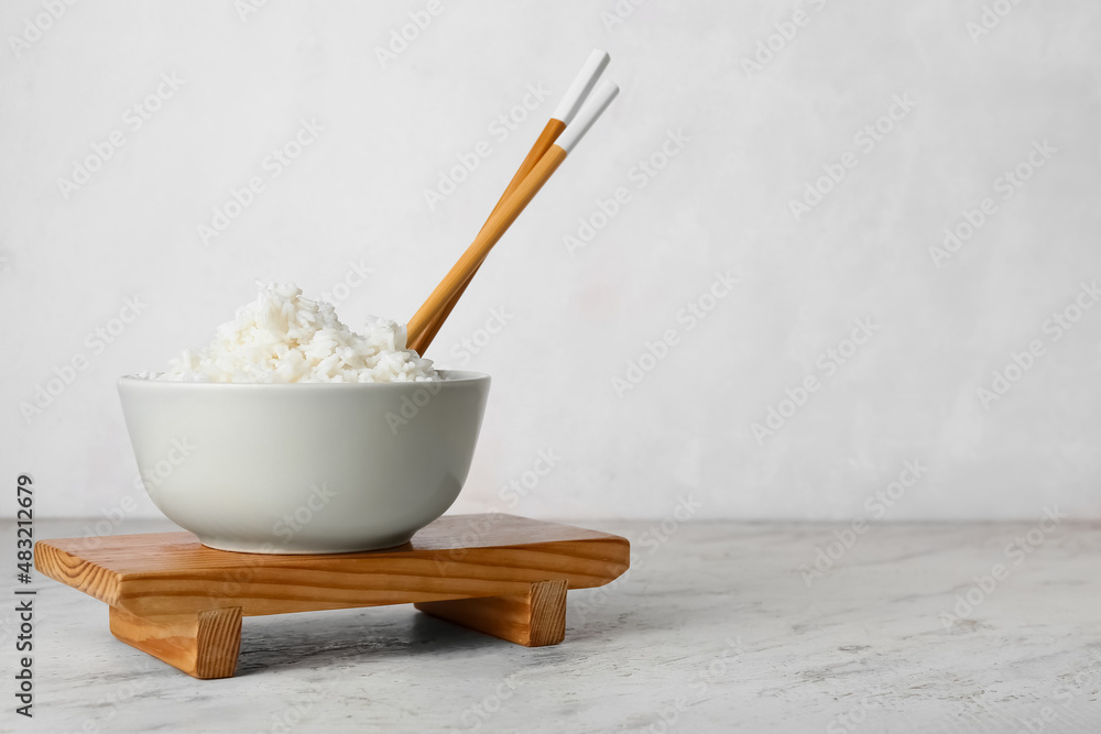 Bowl with tasty boiled rice and chopsticks on light background