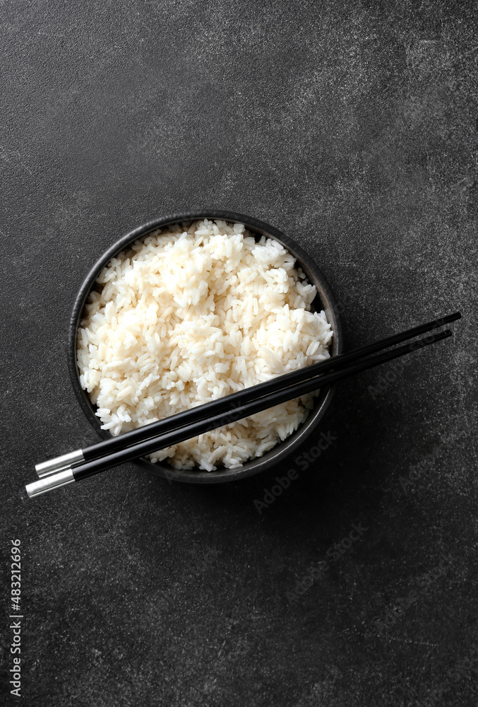 Bowl with tasty boiled rice and chopsticks on dark background