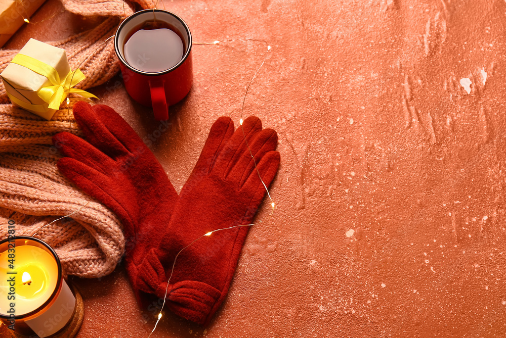 Warm gloves, Christmas lights, Burning candle and cup of tea on red background