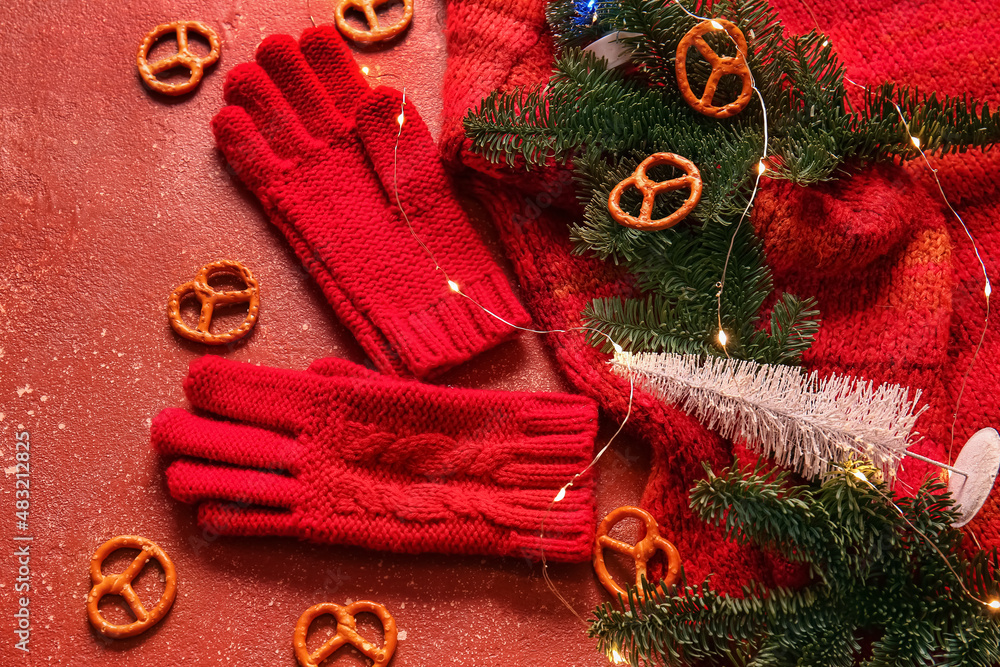 Warm gloves, sweater, Christmas lights and fir branches on red background