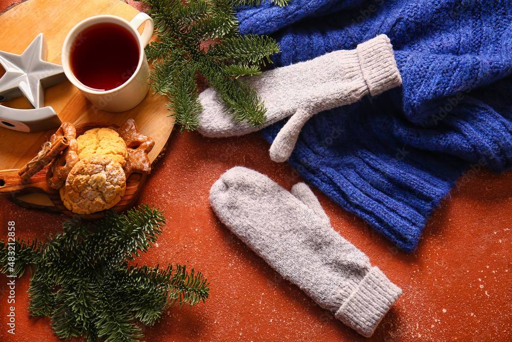 Warm gloves, cup of tea, cookies and fir branches on red background