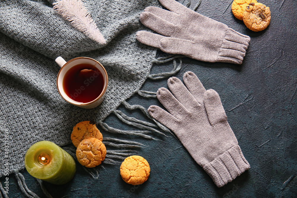 Warm gloves, burning candle, cup of tea and cookies on black background