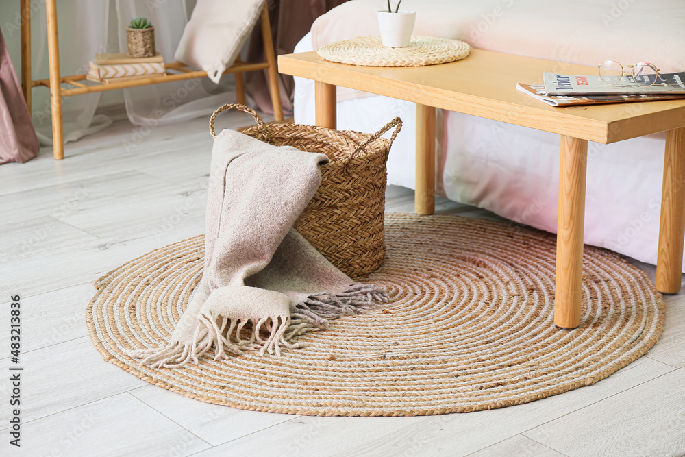 Basket with plaid on wicker carpet in bedroom