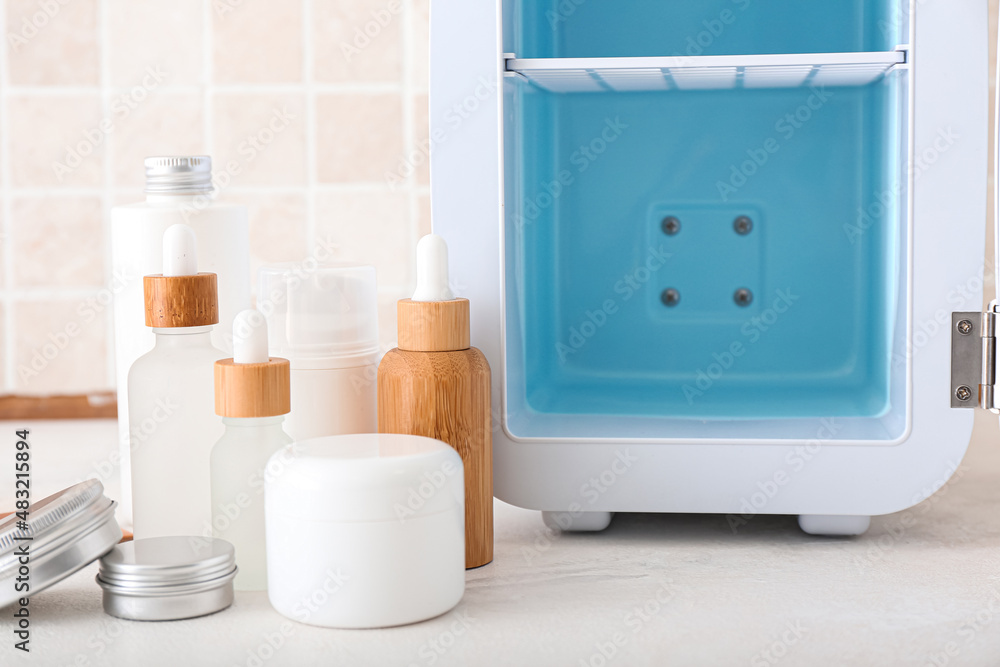 Small refrigerator and cosmetic products on table, closeup