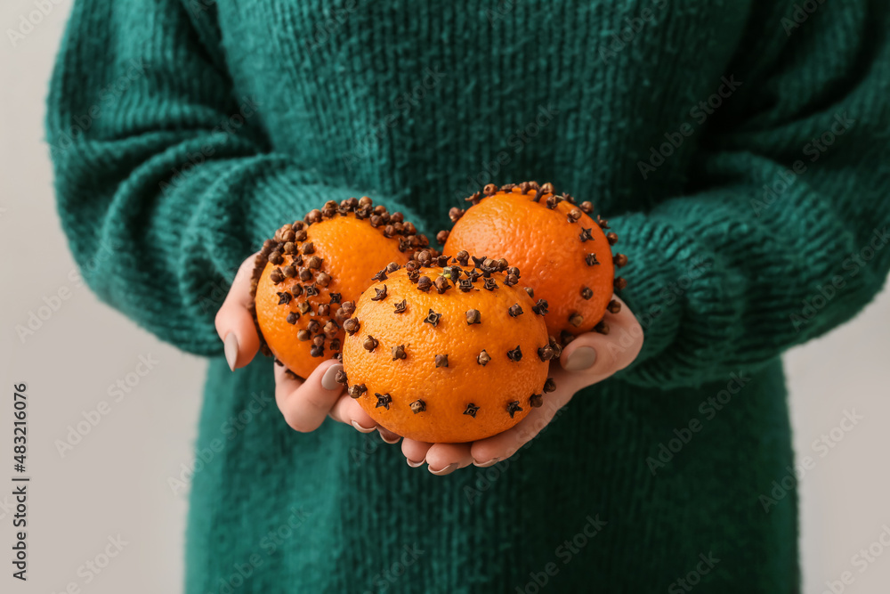 Woman holding handmade Christmas decoration made of tangerines with cloves on light background, clos