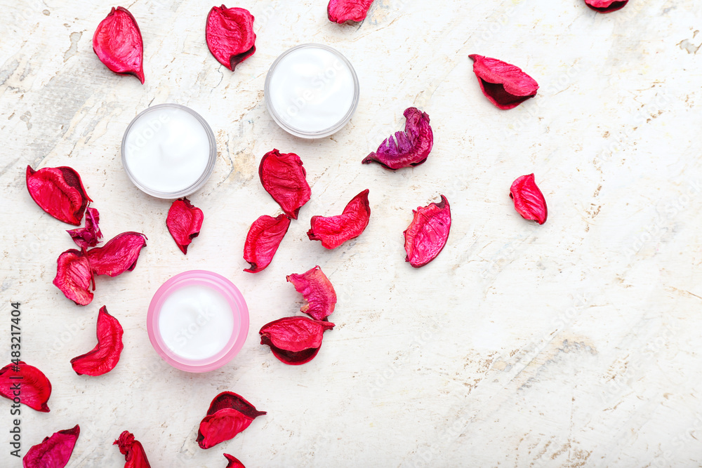 Jars with natural cosmetic cream and rose petals on light background