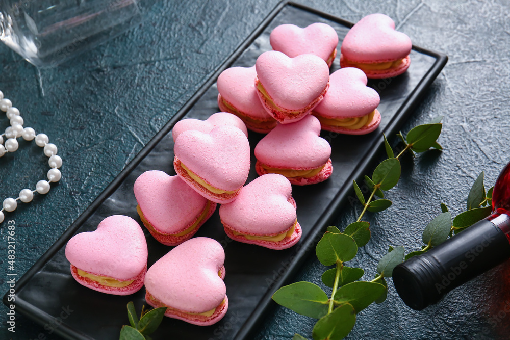 Board with tasty heart-shaped macaroons on black background