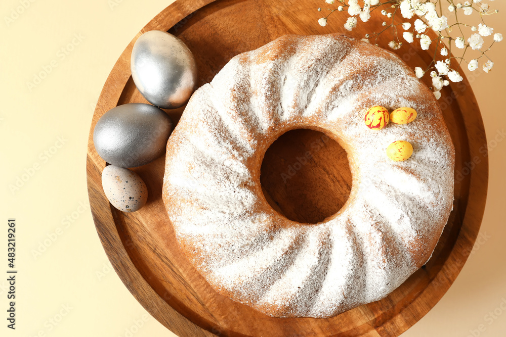 Dessert stand with tasty Easter cake, gypsophila flowers and eggs on beige background