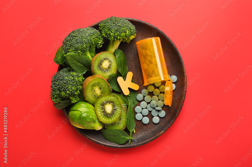 Plate with healthy products, bottle of pills and letter K on red background