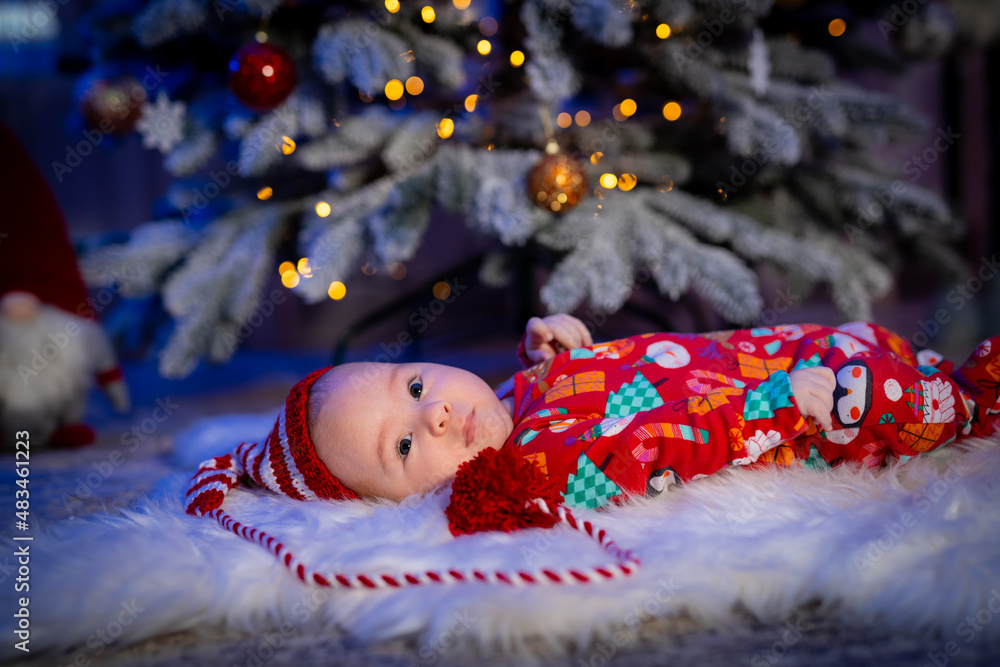 Cute child in Christmas clothes. Baby with lying on the floor. Fur tree at the background. Stock pho