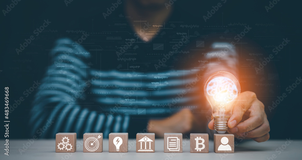 Man hand holding light bulb with Business icon on wood cube and working on desk, Creativity, and inn