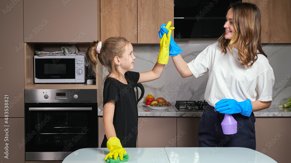 Mother and teen daughter with colorful gloves clean white table with green sponge and cleanser givin