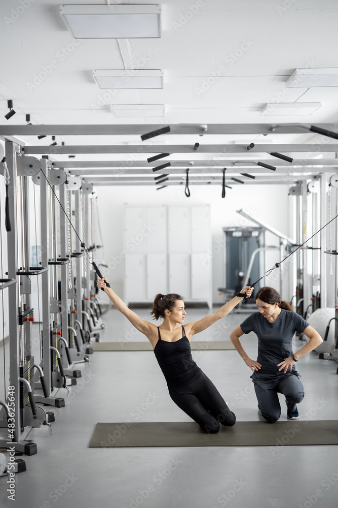 Young woman doing exercises on decompression simulators with the help of rehabilitation specialist. 