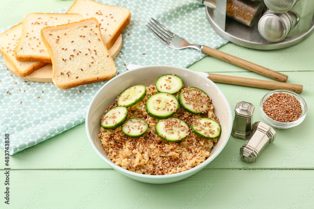 Bowl with tasty oatmeal, flax seeds and cucumber on table