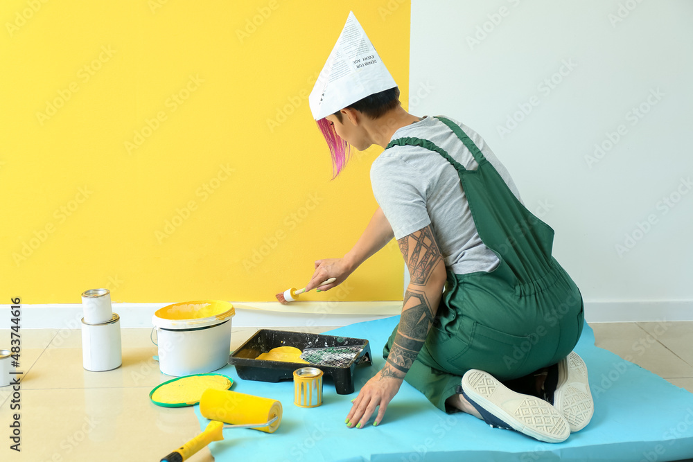 Female decorator painting yellow wall in room