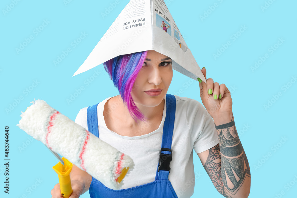 Female painter with paper hat and paint roller on blue background