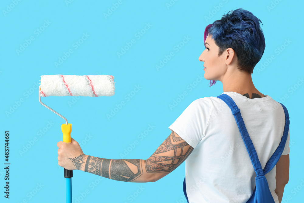 Female painter with bright hair and paint roller on blue background