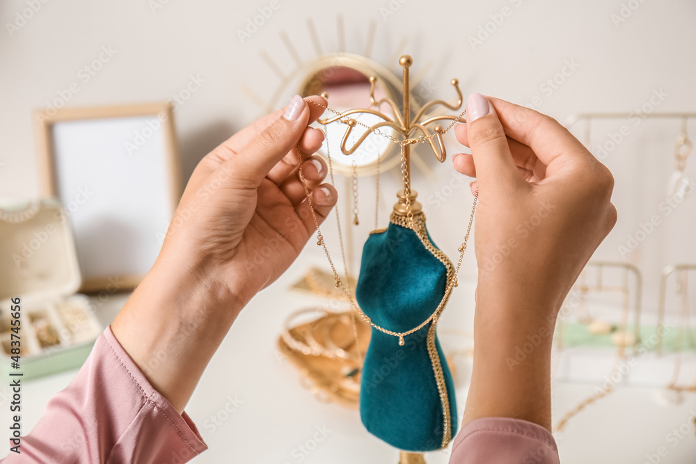 Woman taking stylish necklace from stand on white table, closeup