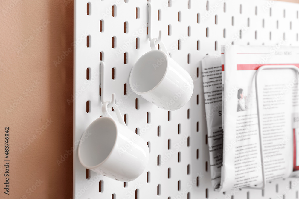 Pegboard with cups on color wall, closeup