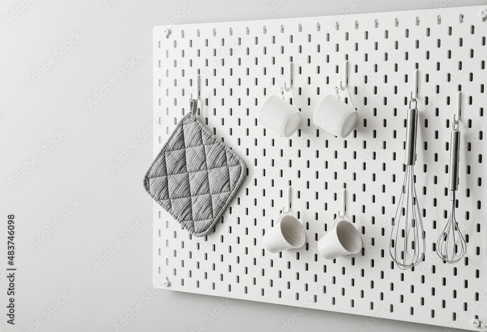 Pegboard with towel, cups and whisks on light wall