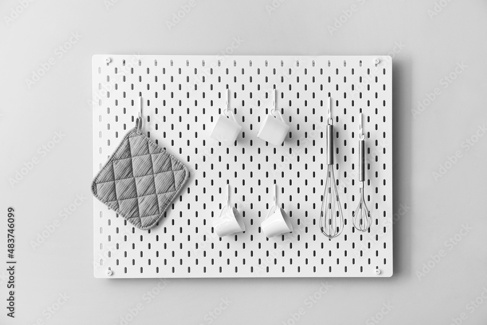 Pegboard with towel, cups and whisks on light wall