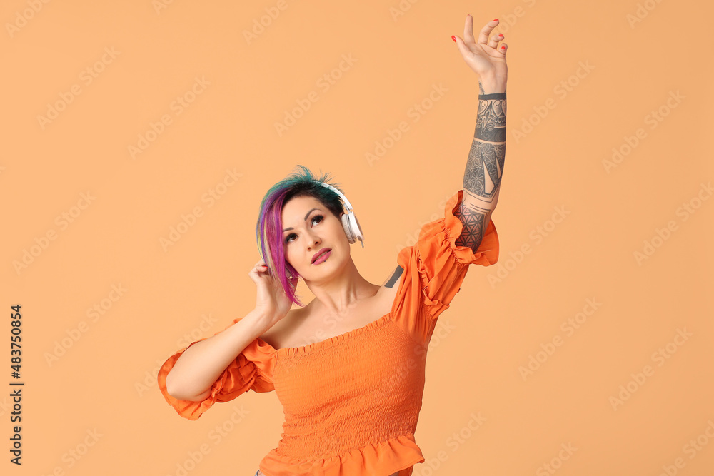 Beautiful woman with unusual hair and tattoo listening to music on orange background