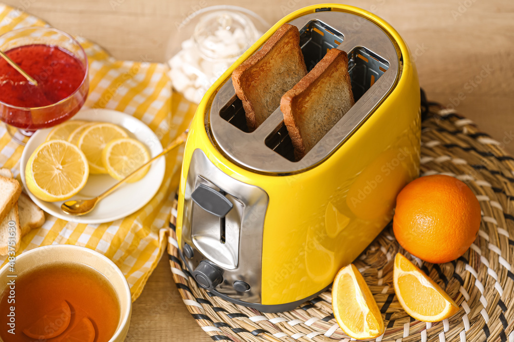 Yellow toaster with bread slices, fruits, cup of tea and jam on table