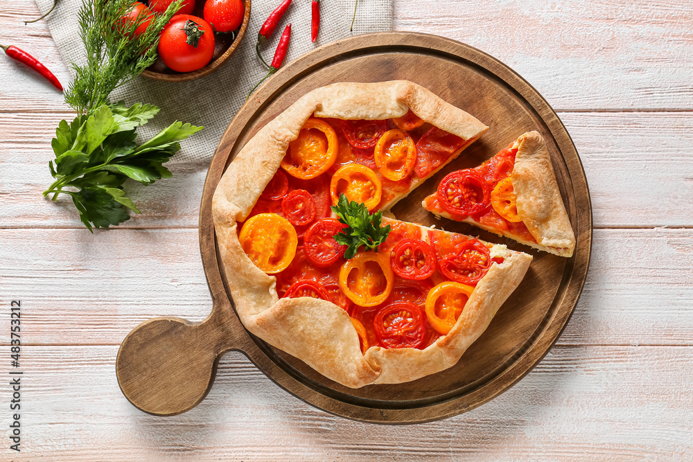 Board with tasty tomato galette on light wooden background